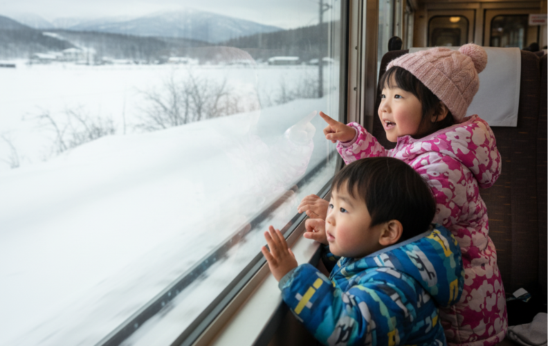 冬の北海道を走るJR列車の車窓から雪景色を見る子供